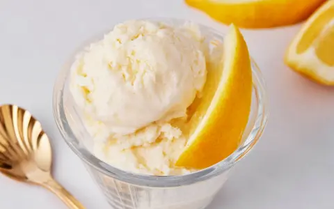 Erfrischendes Zitroneneis selber machen: Cremiges Eis im Glas mit Zitronenspalte und goldener Löffel.