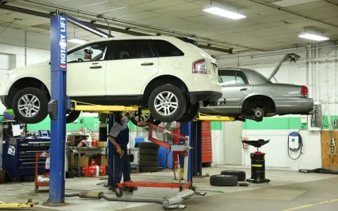 Mecánico trabajando en un taller con vehículos elevados, usando herramientas para neumáticos y otros equipos.