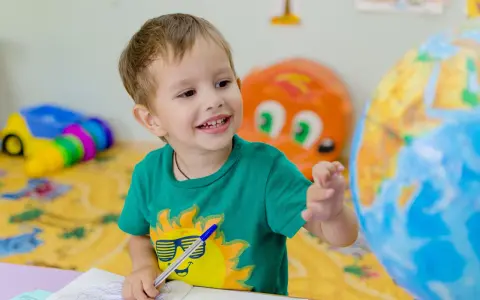 Uśmiechnięte polskie dziecko w hiszpańskiej szkole bawi się globusem i rysuje w zeszycie.