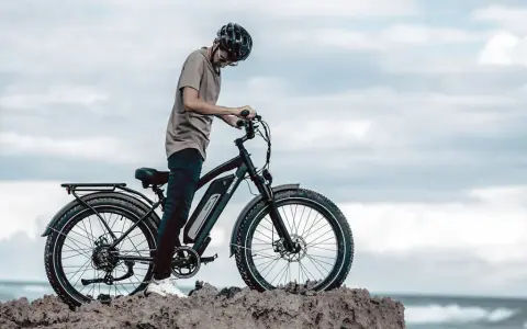 Ein Mann mit Helm steht neben einem Fatbike mit breiten Reifen am Meer. Was ist ein Fatbike? Ein robustes Fahrrad für jedes Gelände.