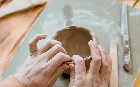 Mani che modellano argilla per creare una ciotola. Utensili da ceramica e un coltello sono visibili. Un ottimo punto di partenza per chi cerca dove trovare l'argilla.