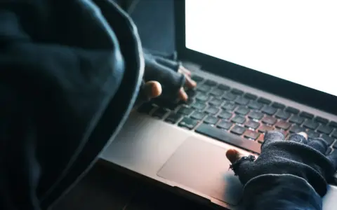 Osoba w kapturze i rękawiczkach pisze na laptopie. To może być przykład kradzieży tożsamości.