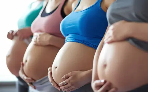 Fyra gravida kvinnor står sida vid sida och håller sina magar. En av dem, andfådd gravid, ler.