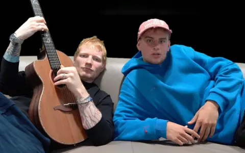 Ed Sheeran z gitarą i Yung Gravy w niebieskiej bluzie. "Azizam, co to znaczy?" - zastanawia się Yung Gravy, patrząc na tatuaże Eda.