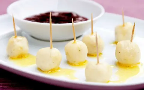 Små, gyllene kroppkakor med tandpetare, serverade med en skål mörk sylt. Ett spännande recept att prova!