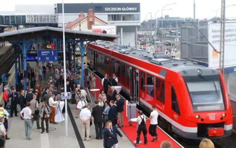 Czerwony pociąg na peronie dworca Szczecin Główny, gotowy do podróży do Berlina. Ludzie czekają na platformie.