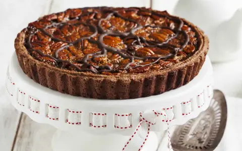 Deliziosa crostata al cioccolato con noci pecan caramellate e un elegante motivo di cioccolato fuso. Perfetta per ogni occasione.