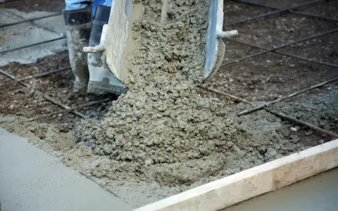 Wylewanie świeżego betonu na zbrojenie. Trwa naprawa betonu, widać buty pracownika i metalowe pręty.