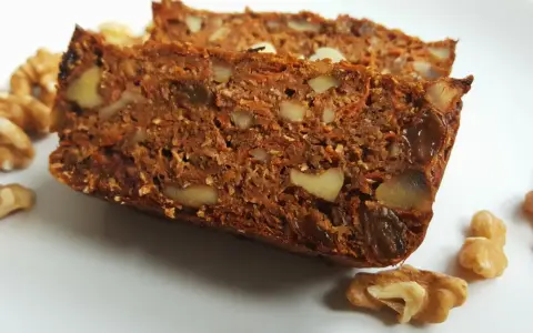 Dwa kawałki ciasta marchewkowego fit z orzechami włoskimi i rodzynkami na białym talerzu.