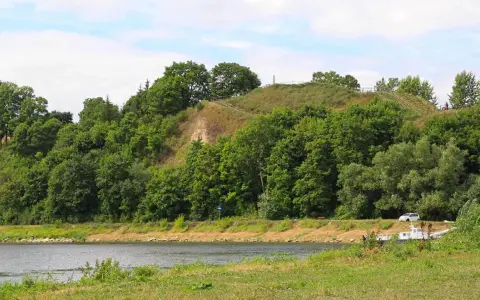 Zielona skarpa nad rzeką, na szczycie której widać ścieżki i ogrodzenie. To góra zamkowa w Drohiczynie, miejsce pełne historii.