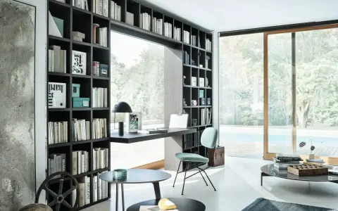 Libreria a muro con scrivania integrata, perfetta per idee stanza studio piccola. Sedia azzurra, tavolini neri e vista piscina.