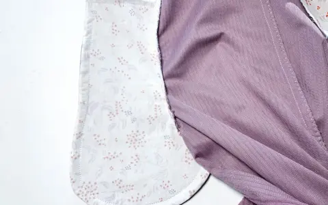 Détail d'un vêtement en cours de confection, montrant la doublure à motifs floraux des poches italiennes et le tissu extérieur violet.