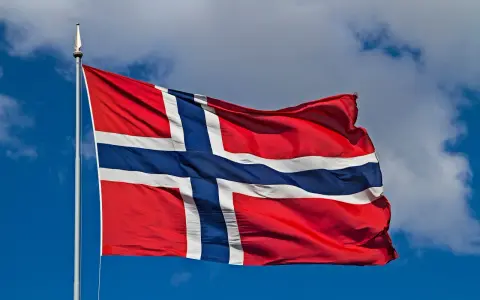 Norweska flaga powiewa na wietrze. W tle błękitne niebo z chmurami. Takie są prace, gdy jest piękna pogoda.