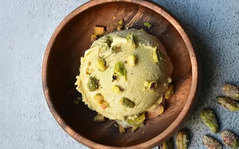 Cremoso helado de pistacho con trozos de pistacho en un cuenco de madera.