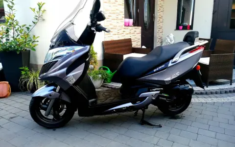 Elegancki skuter Kymco Dink 50 w kolorze grafitowym stoi na podjeździe, gotowy do jazdy.