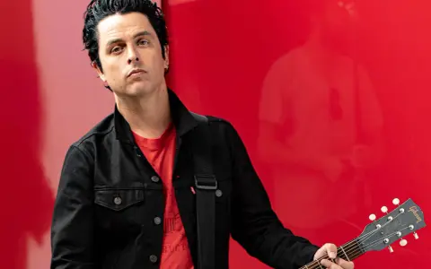 Billie Joe Armstrong, green day sångare, med sin Gibson Les Paul gitarr mot en röd bakgrund.