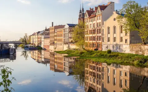 Nad rzeką w Opolu, w blasku słońca, odbijają się kamienice. To jedne z wielu magicznych miejsc opolskich, które zachwycają spokojem i pięknem.
