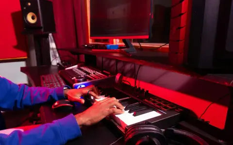 Les mains d'une personne jouent sur un clavier, entourées d'équipement de studio, un rêve de devenir beatmaker.