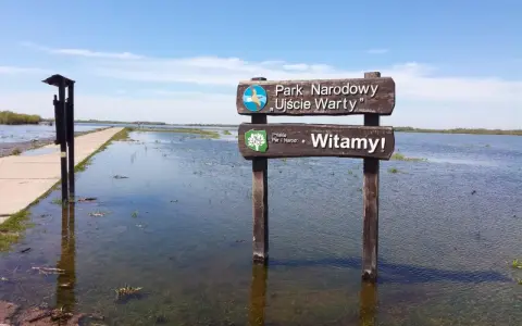 Witaj w polskim parku narodowym Ujście Warty! Droga zalana wodą, a obok tablica powitalna.