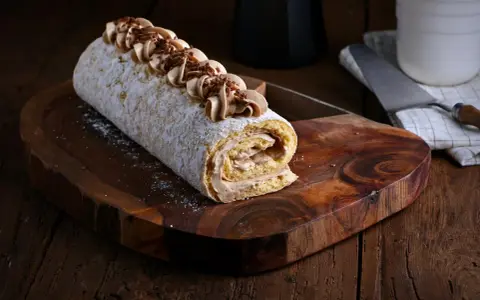 Un delicioso brazo de gitano cubierto de azúcar glas y decorado con crema de café y virutas de chocolate, listo para ser servido.