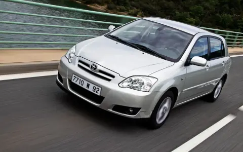 Srebrna Toyota Corolla 2004 na moście, z widokiem na wodę i las.