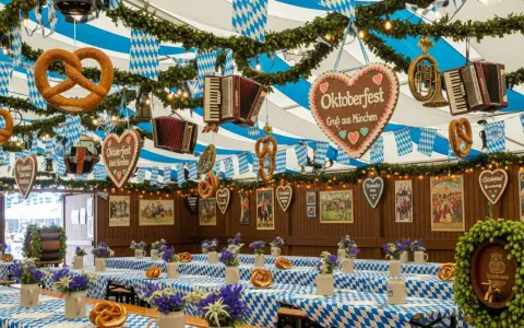 Wnętrze namiotu na Oktoberfest w Monachium. Wiszące precle, serca z piernika i akordeony. Stoły przykryte niebiesko-białymi obrusami, ozdobione kwiatami i kolejnymi preclami.