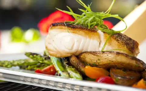 Aromatyczny halibut na talerzu z pieczonymi ziemniakami, szparagami i pomidorkami. Zapach halibut na jakie ryby?