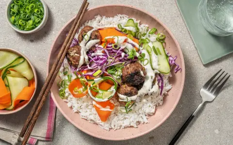 En skål med ris, köttbullar, strimlad rödkål, morötter och gurka, toppad med en krämig sås. En härlig vietnamesisk matupplevelse.