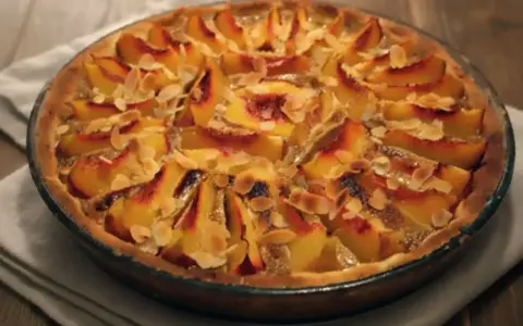 Tarte aux pêches amande, une gourmandise dorée aux fruits fondants et éclats d'amandes effilées, prête à être dégustée.