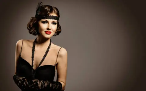Elegancka kobieta w stylu makijaż lat 20., z opaską na głowie i czerwoną szminką, w czarnej sukni i koronkowej rękawiczce.