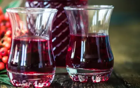 Dwa kieliszki wypełnione rubinową nalewką z czeremchy, obok butelka i kiść owoców.
