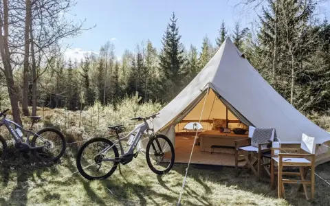 Två elcyklar står redo för äventyr vid ett stort tält på Bengts camping. Skogen bakom bjuder in till utforskning.