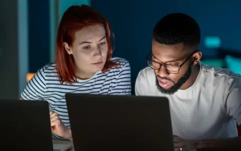 Zwei Personen arbeiten konzentriert an Laptops. Sie besprechen Details, vielleicht für einen partnerschaftsvertrag ohne notar.
