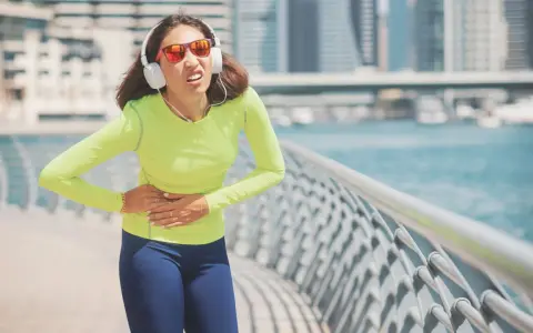 Une coureuse en tenue de sport, écouteurs aux oreilles, se tient le ventre, visiblement prise d'un point de côté.