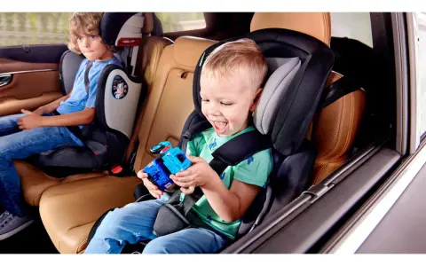 Uśmiechnięty chłopiec bawi się zabawką w foteliku Kinderkraft Comfort Up ADAC. Obok siedzi starszy brat.