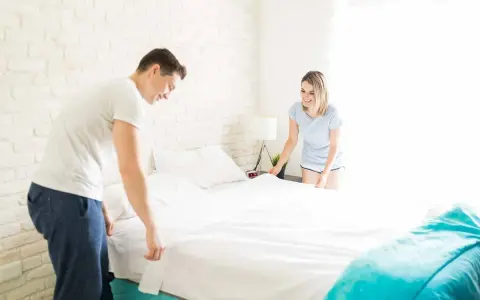 Coppia sorridente che collabora per rifare il letto con piumone, creando un ambiente accogliente.