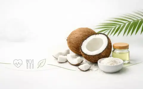Cały i połówka kokosa, kawałki miąższu, wiórki kokosowe, olej kokosowy w słoiczku i liść palmy. Kokos to orzech, który oferuje wiele zdrowych produktów.