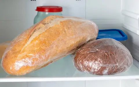 Deux pains emballés dans du film plastique, un pain blanc et un pain brun, sont rangés dans le frigo.
