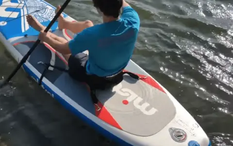 Mann sitzt auf SUP-Board, paddelt und befestigt den Sitz.
