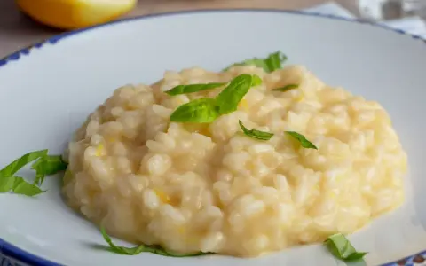 Kremowe, letnie risotto z cytryną i bazylią, podane na białym talerzu z niebieskim rantem.