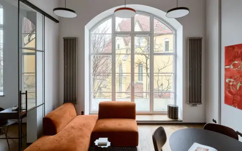 Nowoczesny salon z pomarańczową kanapą, czarnym stolikiem i obrazem. Jakie dodatki podkreślają styl?