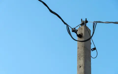 Betonowy słup energetyczny z przewodami na tle błękitnego nieba. Zastanawiasz się, ile za słup energetyczny na działce?