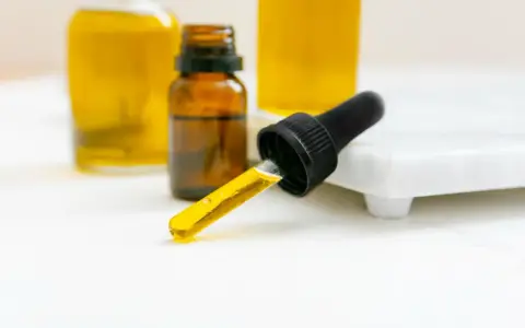Kropla olejku z pipety, obok buteleczek z żółtym płynem. Czy to patchouli?