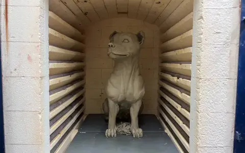 En hundskulptur i blålera keramik väntar på att brännas i en ugn.