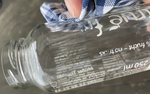 Mit einem Tuch wird das "true fruits" Schrift entfernt. Die Flasche ist aus Glas und hat einen Pfandaufdruck.