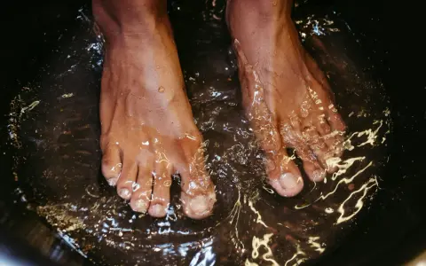 A close-up of feet soaking in a dark basin, likely a relaxing foot bath with epsom salt for feet.