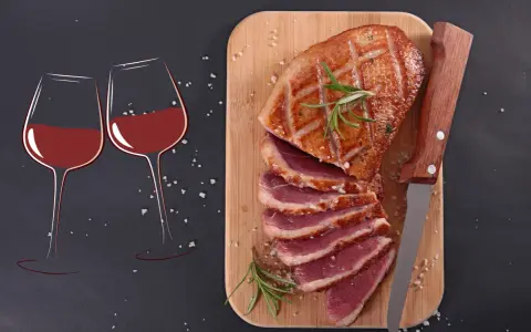 Quel vin avec magret de canard ? Deux verres de vin rouge et un magret de canard tranché sur une planche en bois, prêts à être dégustés.