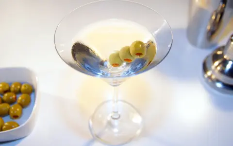 Kto wybierze Dirty Martini czy klasyczne Dry Martini? Kieliszek z oliwkami i drinkiem na białym tle.