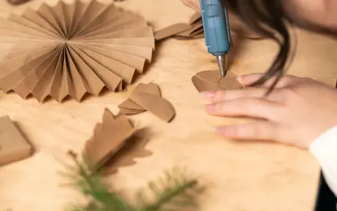 Manos creando manualidades con cartón para adultos. Se usa una pistola de silicona para pegar piezas de cartón, formando adornos.