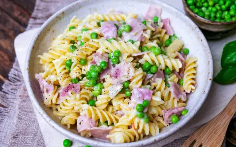 Fusilli-Nudeln mit Erbsen und Schinken in einer cremigen schinken sahne sauce, bestreut mit schwarzem Pfeffer.